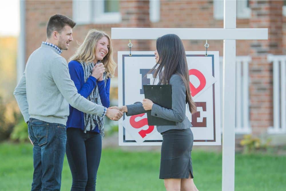 Couple shaking hands with a real estate agent in from of a sold sign